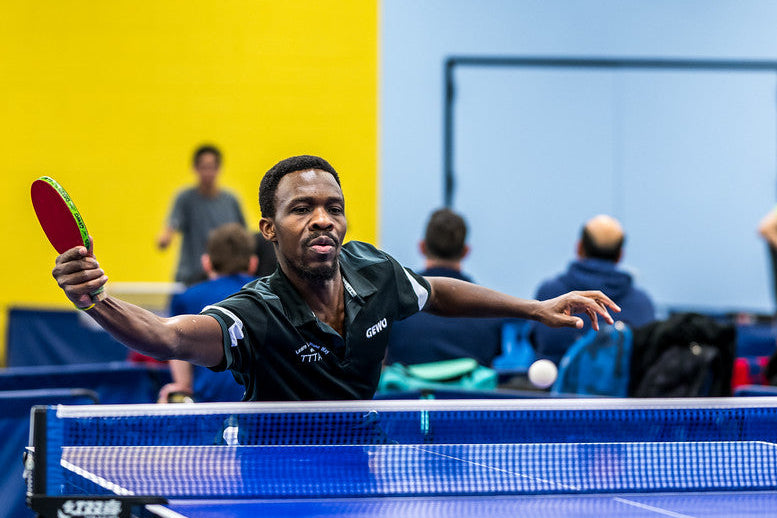Man playing table tennis in an indoor setting with a blue and yellow wall.